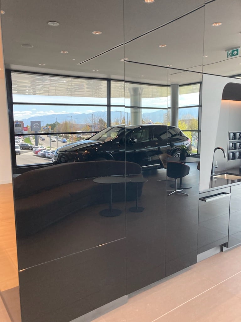 Black glass partition wall reflecting a black SUV in a car showroom